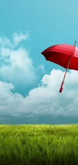 Red umbrella floating in blue sky with fluffy clouds and green field.