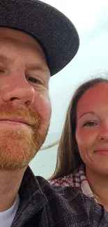 Couple taking a selfie under a red umbrella by the seaside.