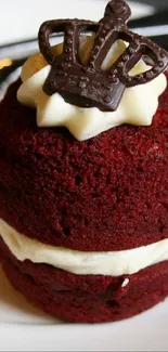 Red velvet cupcake with frosting and crown on a plate.