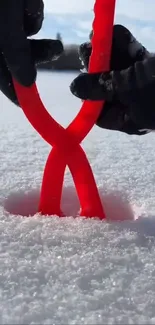 Hands holding red yarn in snowy landscape.