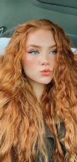 Red-haired woman poses in car with vibrant, natural curls.