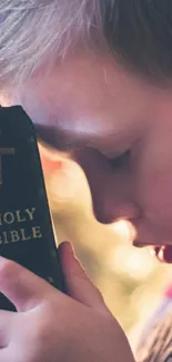 Child in prayer holding a Bible wallpaper.