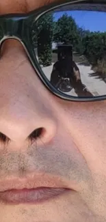 Close-up of face with reflective sunglasses showing outdoor scene.