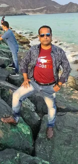 Man posing on rocky beach shore in front of turquoise ocean.