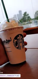 Person holding a Starbucks cup with an outdoor backdrop.