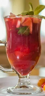 Glass of red fruit beverage with mint garnish on a plate.