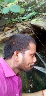 Man drinking from a natural stream in the forest.