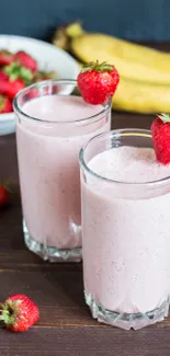 Two glasses of pink strawberry smoothies with fresh fruits.