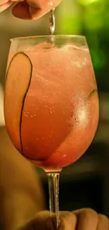 Refreshing pink cocktail in a glass with cucumber slices, green background.