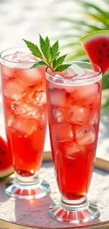 Two tall glasses of watermelon drink on a sunny beach.
