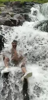 Person enjoying a refreshing cascade of waterfall, seated on rocky terrain.