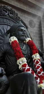 Regal statue adorned with a red and white garland on a mobile wallpaper.