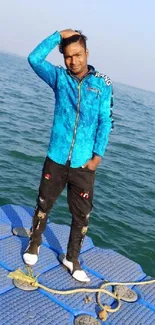 Person in blue jacket standing on a dock by the ocean.