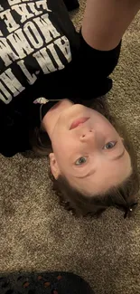 A child lying on a brown carpet wearing a black graphic tee.