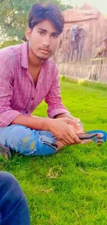 Young man in casual attire sitting on a green lawn.