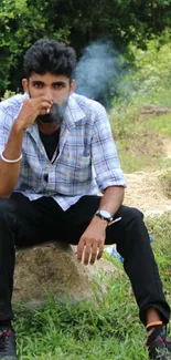 Man sitting on rock in nature, exhaling smoke.