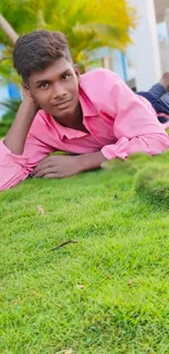 Young man in pink shirt relaxing on green grass outdoors.