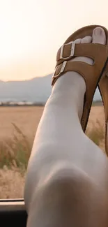 Legs in sandals out car window during sunset road trip.