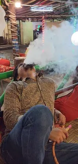 Person relaxing in lounge with hookah amid atmospheric smoke.