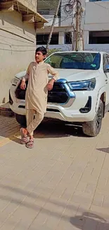 Boy in traditional clothing leaning against a car.