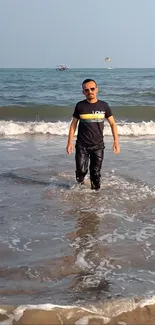 Man walking on a sunny beach with ocean waves.