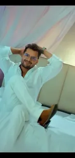 Man lounging on bed in white-themed bedroom.