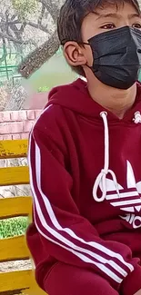 Child in maroon hoodie on yellow bench in a park.