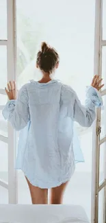 Person in blue shirt opens door to a peaceful morning view.