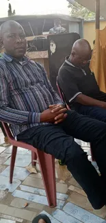 Two men sitting outdoors on plastic chairs during a casual gathering.