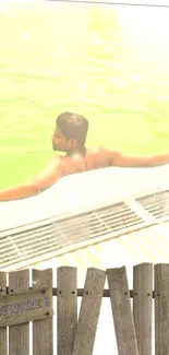 Man relaxing in a vibrant pool with wooden fence.