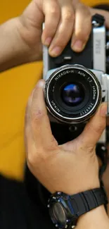 Person holding a vintage camera with a vibrant yellow background.