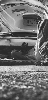 Mechanic working under classic vintage car in grayscale wallpaper.