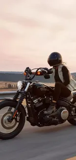 Biker rides motorcycle at sunset on scenic highway.