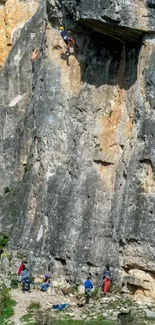 People rock climbing on a large cliff face, set in a natural landscape.