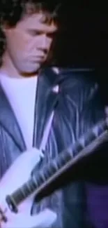 Guitarist in black leather jacket playing a white electric guitar on stage.