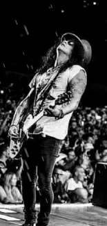 Black and white photo of a guitarist rocking out on stage in front of a large crowd.