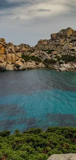 Rocky coastline with teal blue waters under a cloudy sky.