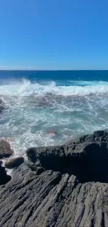 Dynamic rocky beach with crashing ocean waves under a clear blue sky.