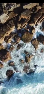 Aerial view of rocky shoreline with ocean waves crashing on stones.