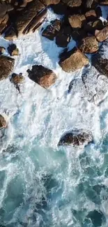 Aerial view of waves crashing on rocky shoreline with blue water texture.