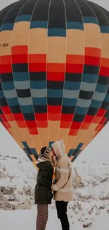 Couple embracing under a colorful hot air balloon in a snowy landscape.