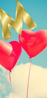 Two red heart balloons with gold letter on blue sky background.