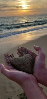 Hands holding heart-shaped sand at sunset on the beach.