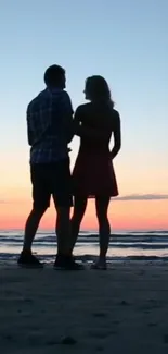 Silhouette of a couple against a colorful sunset on a beach.