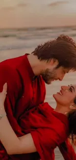 A couple in red embraces romantically on a beach at sunset.