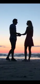 Couple holding hands at sunset on a beach, creating a romantic silhouette.