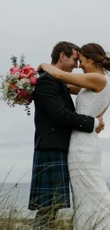 Couple embracing at beach wedding with floral bouquet