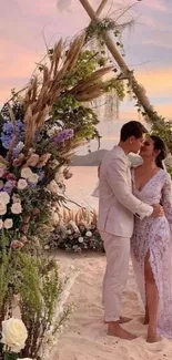 Romantic couple at beach wedding under floral arch at sunset.