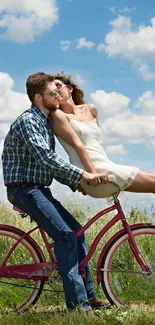 Couple kissing on a pink bicycle in a grassy field under a blue sky.