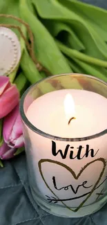 Candle with love, pink tulips, and heart decor on a grey quilted background.